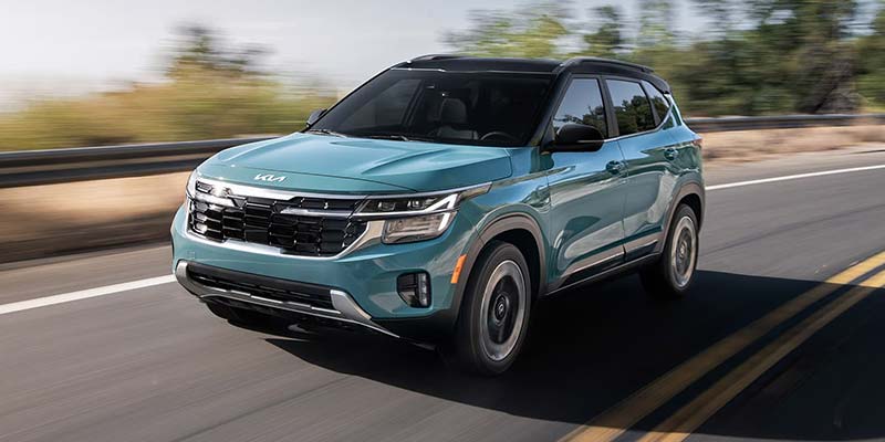 Teal Kia Seltos SUV driving on a scenic countryside road.