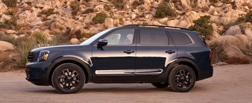 Dark blue Kia Telluride SUV parked on a rugged desert road with rocky hills in the background.